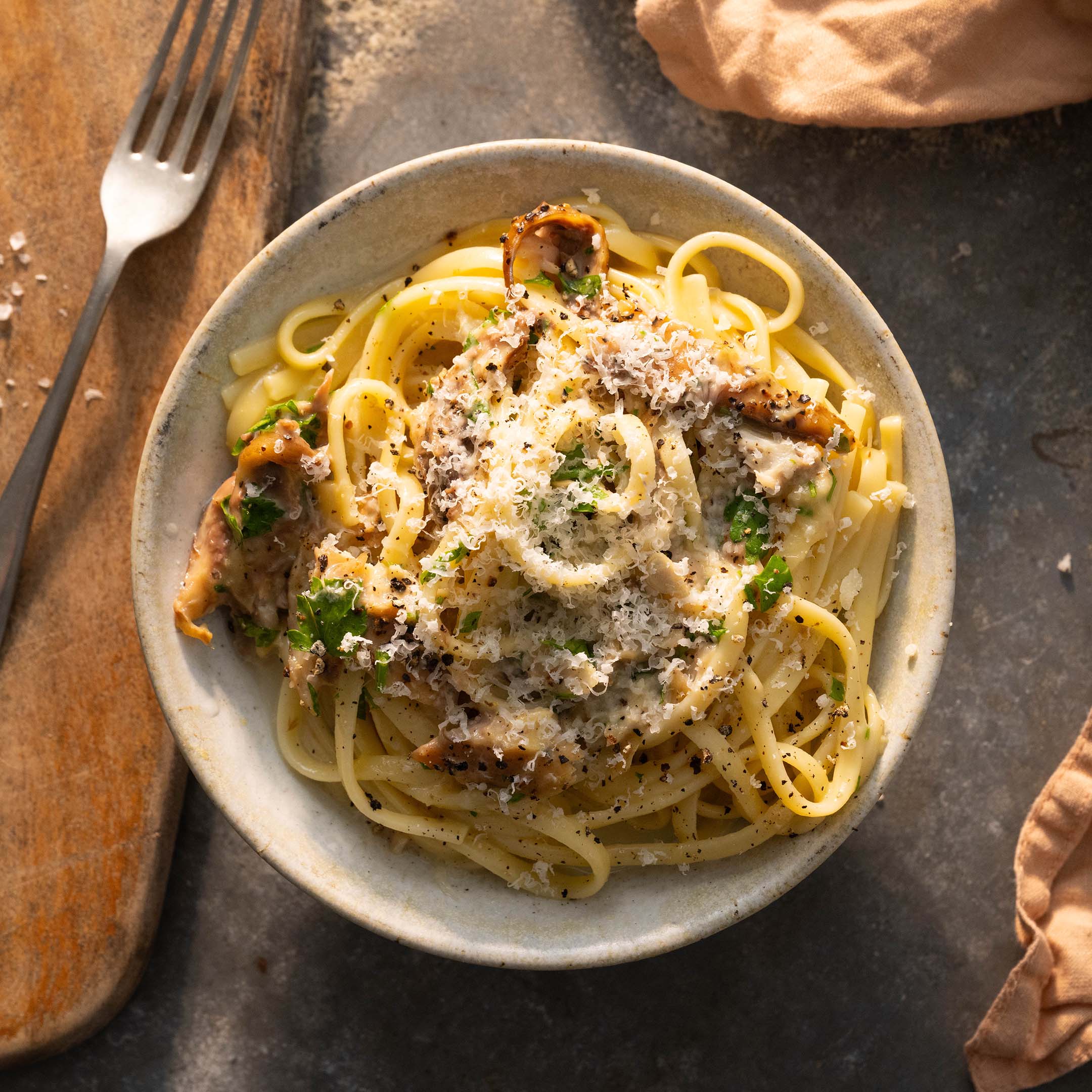 A bowl of smoked mackerel carbonara sits on a granite table with a wooden chopping board to the left hand side.